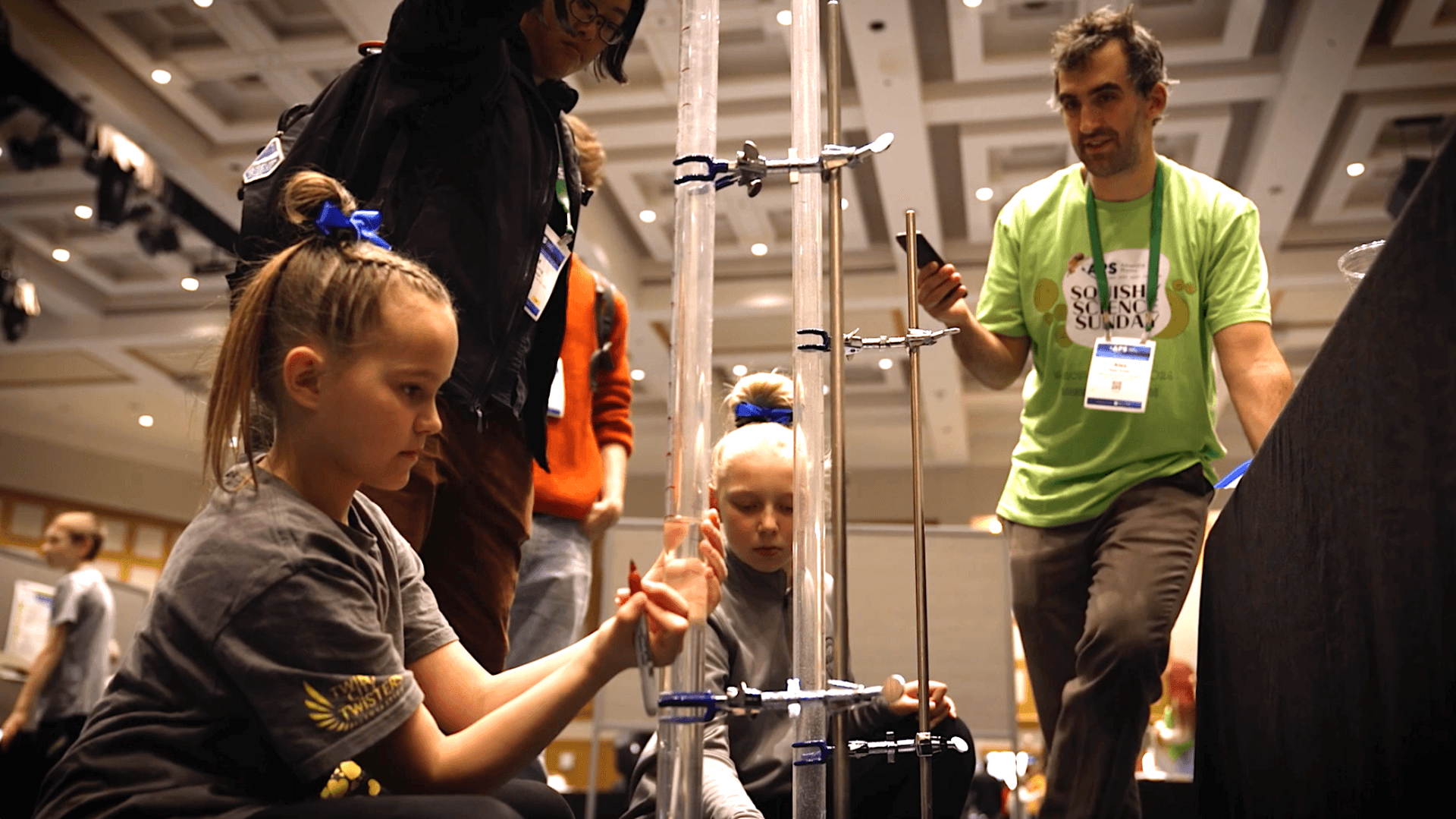 A girl crouches in front of a science instrument as a volunteer looks on.