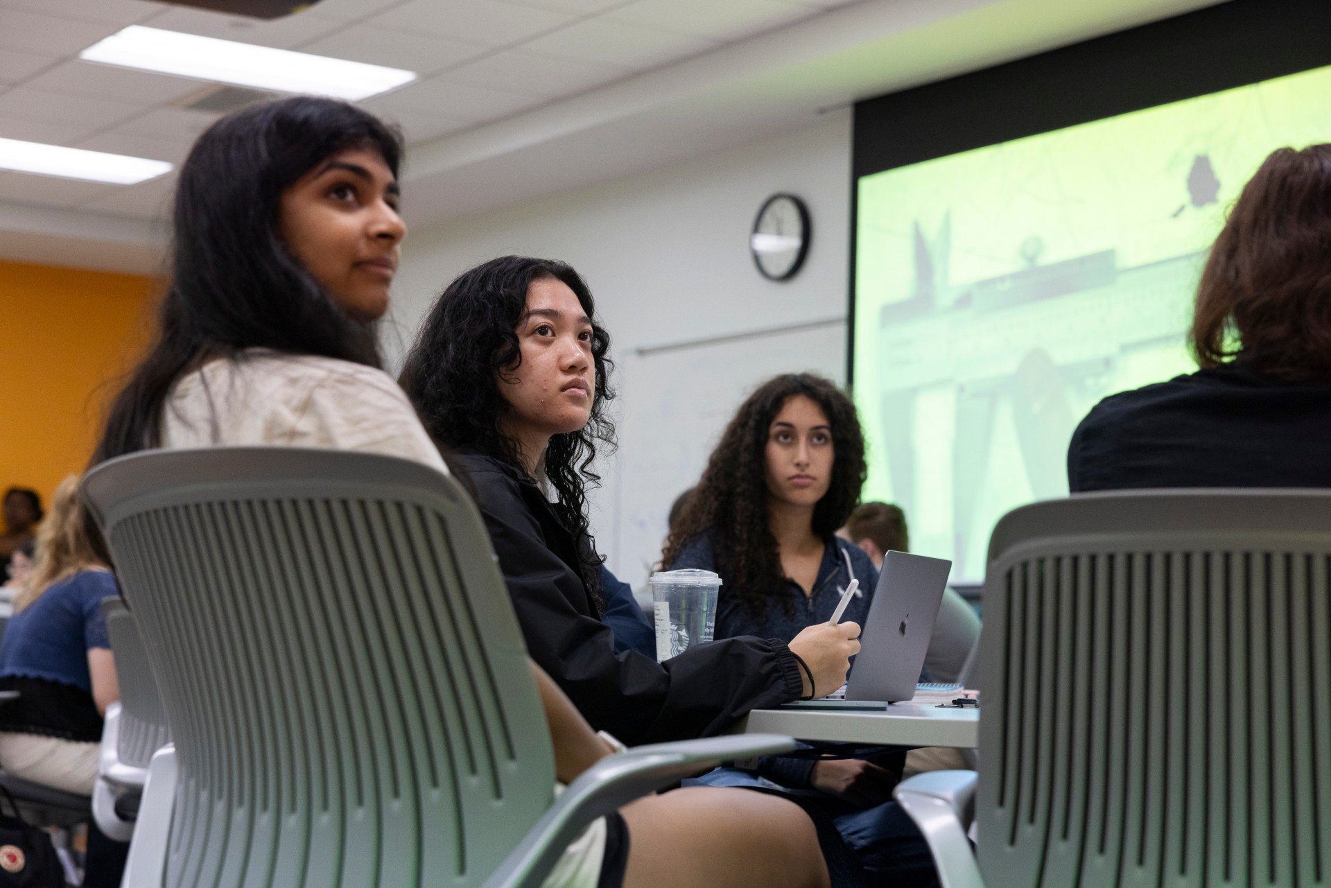 Students listen to a presentation at a table in a physics lab