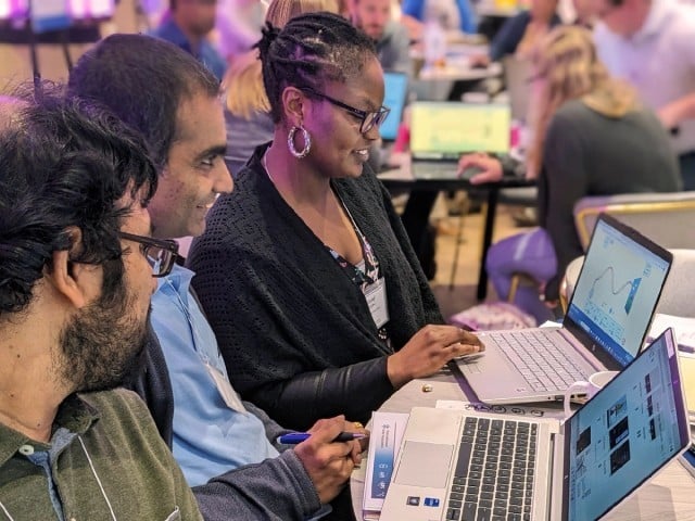 A Black woman, a Southeast Asian man, and another man looking at a chart on a computer together