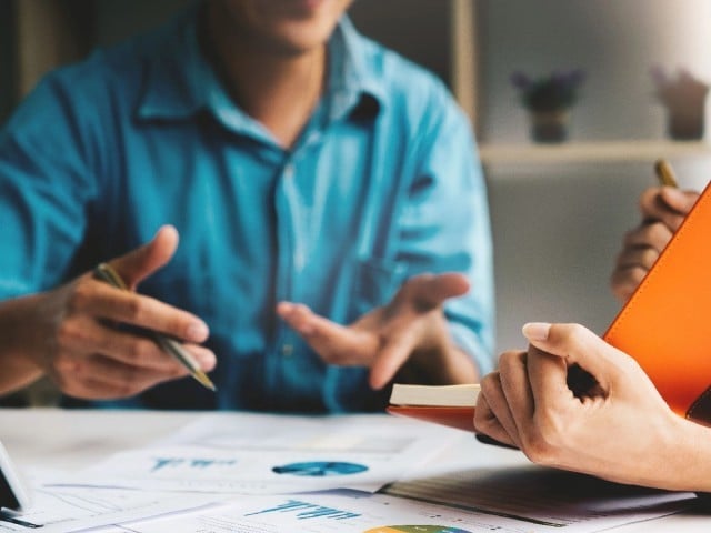 A man and woman discussing and taking notes over printed charts and graphs